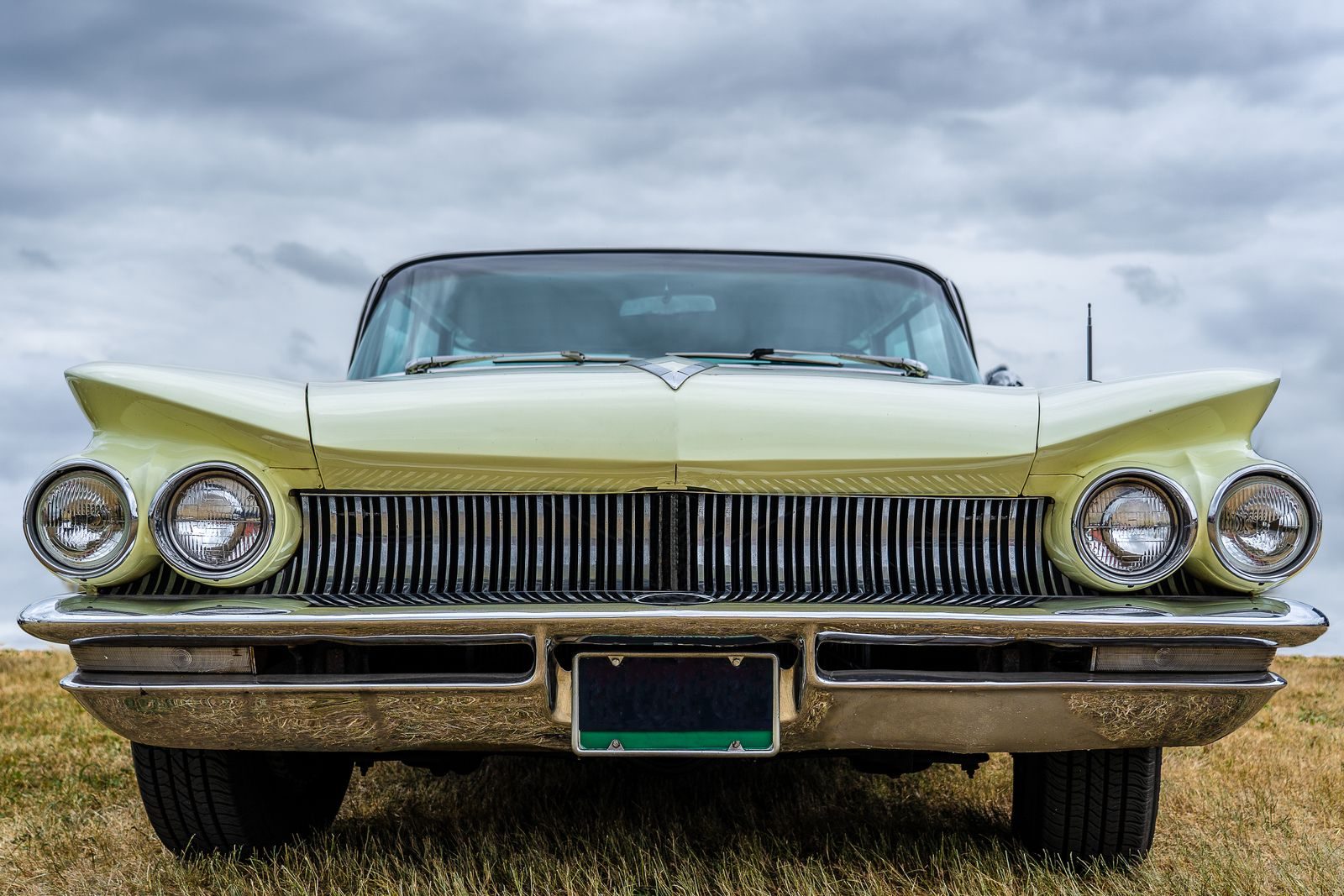 Front view of a vintage classic car with chrome trim and a licence plate, parked on grass at an outdoor car show